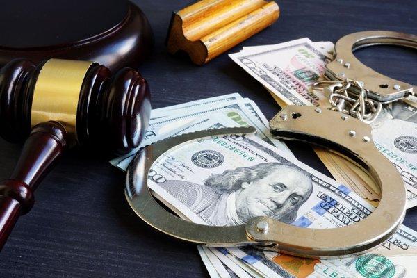 A gavel, handcuffs, and money on a table representing a bail bonds - something held by the court in lieu of the defendant's pretrial