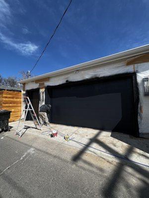 Painting garage doors with a black coat. White brick is all covered with paper and plastic.