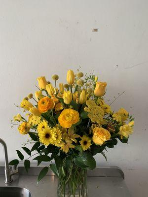 Runuculus, Tulips,Alium, Brighton Roses, Alstromeria, Daisies, Yarrow, Oncidium Orchids, Italian Ruscus, and Salal in a glass Vase