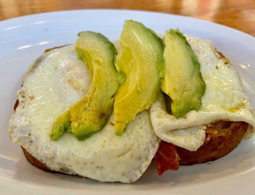 Open faced breakfast sandwich. There's bacon & cheddar below the fried eggs and avocado.