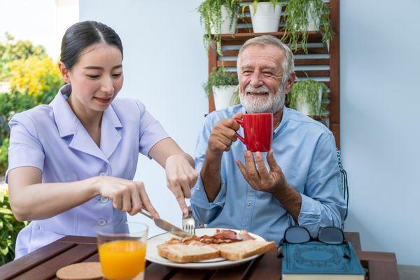 Companions-in-caring-personnel-assist-elderly-senior-man-eat-breakfast-happily