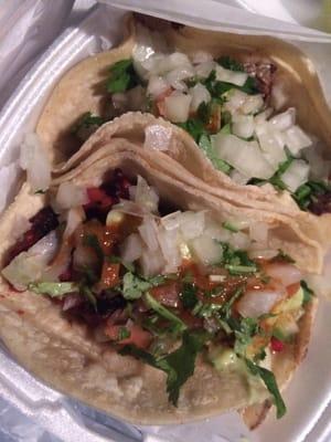 Carne asada (steak) taco and roasted pork taco with guac, pico, lettuce, medium salsa, cilantro, onions, and lime on the side.