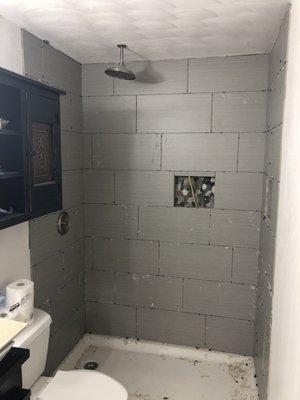 Walk in shower with repositioned shower head and tiled shelves