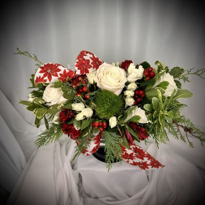 Fresh white Roses pair with berries of the season and seasonal evergreens presented in a glass vase wrapped with a seasonal ribbon.