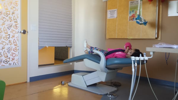 Baby girl in the dental chair with headphones and a TV above her.