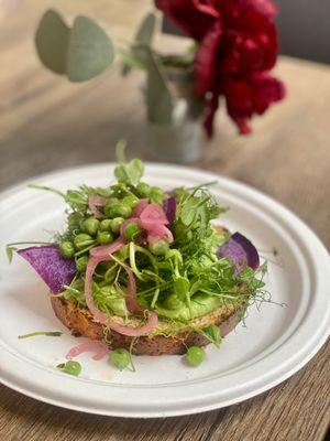 Delicious toast made with an exceptionally fresh slice of bread, pea purée, pickled onions, peas, sprouts, etc.