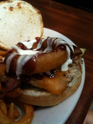 An onion ring atop a cheeseburger dripping with BBQ sauce and ranch dressing