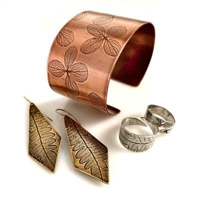 Nature impression jewelry in copper, brass and sterling silver. Hydrangea flowers, ferns, feathers and branches are pressed into the metals.