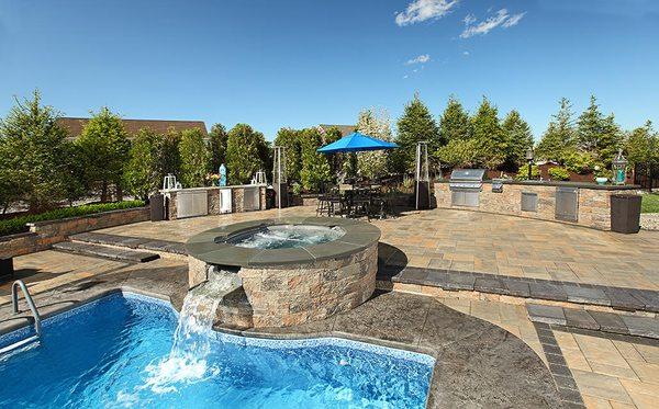 Backyard stone patio with outdoor kitchen and pool design.