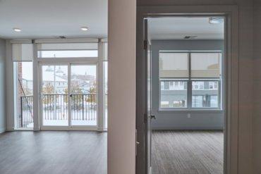 View of the spacious living area, balcony with sliding glass doors, and one of two bedrooms in apartment 2-B.