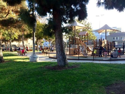 Side of the park with the playground as well as some picnic tables on the far left. Basketball court is behind the playground.