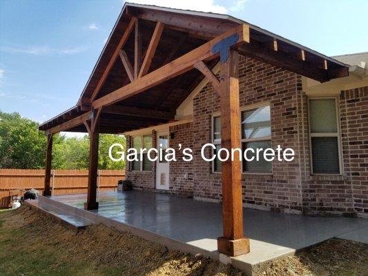 Patio cover peak on side then flat roof.  Cedar wood with stain. Regular brush finished concrete with step on side.