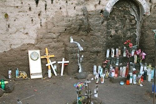 Crosses, candles and personal memorabilia decorate the area. The ground & shrine walls are saturated with candle wax.