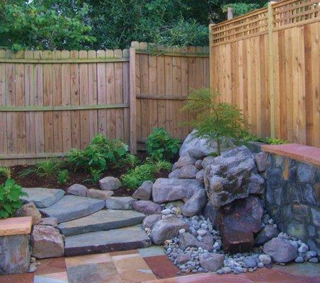 Boulder water feature and stone steps up to back garden