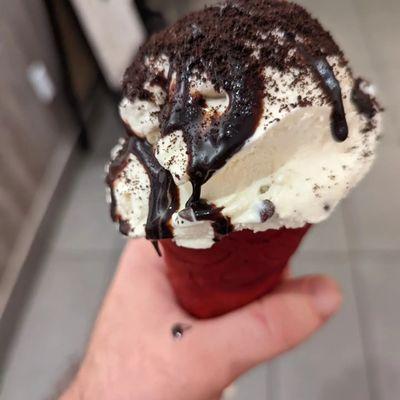 Cookie dough in a red velvet waffle cone with chocolate syrup and orea cookie dust on top