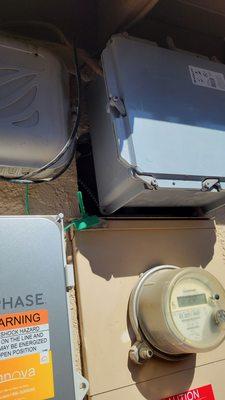 J-box mounted on top of hole opened in exterior wall above electric meter.