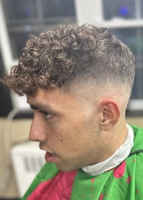 Mid drop Fade with textured curly top meticulously scissor cut , textured , and styled. With gradual length in front for styling.