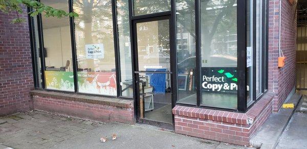 Still waiting to get our sign up!  DESCRIPTION: Street view of windows and glass door of retail shop with Perfect Copy & Print exterior sign