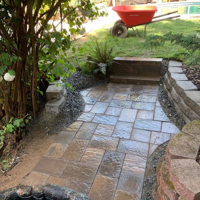 An after picture of beautiful pavers layed by a fountain & garden area as well as a retaing to create a sitting area.