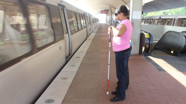 A woman with a white cane waiting for the Metro at the station platform.