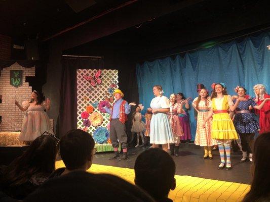 Wizard of oz play. Good witch on left, and colorful munchkins in center