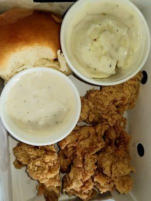 Chicken strip meal with mashed potato and a roll.