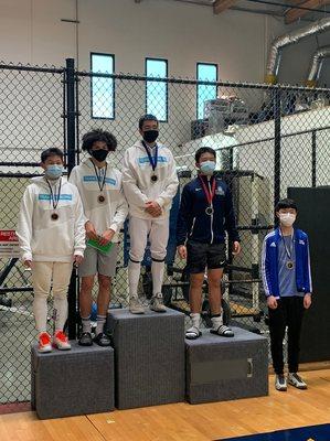 Three fencers of team K stand on podium