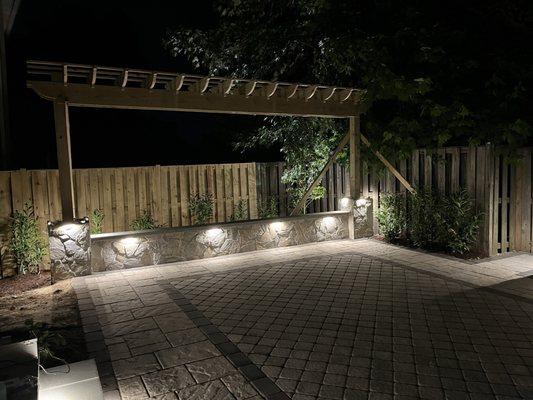 Island with built-in grill and cooktop. Paver patio. seating wall with trellis. Hardscape and Landscape lighting.