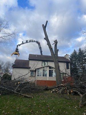 The crane reaching over a house and cutting it down out back by remote control