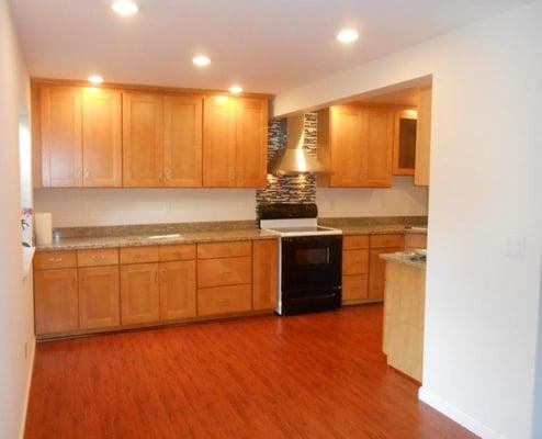 A finished product with brand new cabinetry, granite counter tops, laminate wood flooring, fixtures, tiled back splash, and ligh