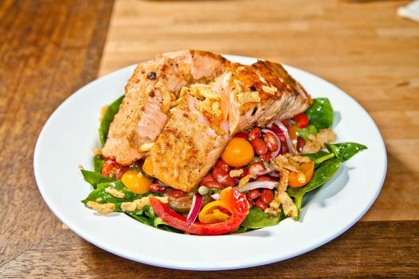 Seasoned pan seared salmon served over fresh spinach, capers, bell peppers, cherry tomatoes, and beans tossed in garlic-basil dressing