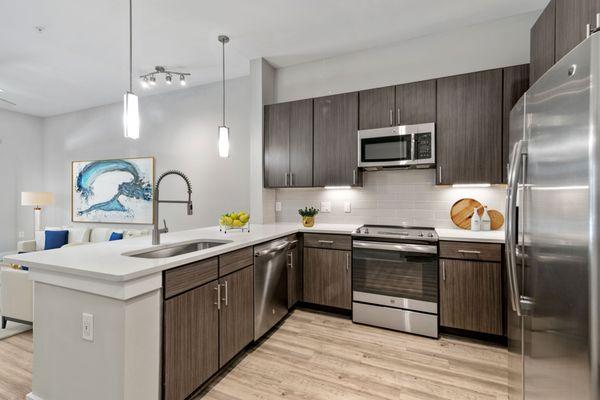 Kitchen with quartz counters, wood-style flooring, dark-colored cabinets, and stainless steel appliances at Lantower Weston Corners.