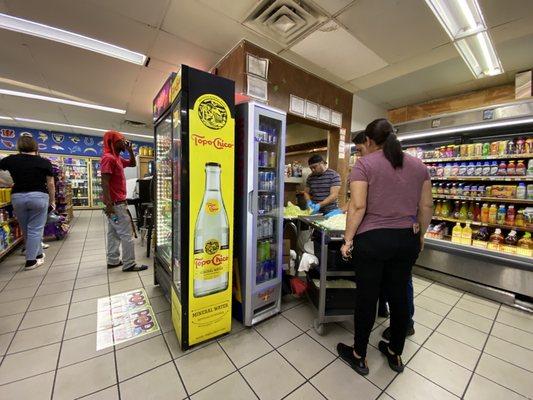 Food preparation outside the kitchen area, with customers walking behind to grab items from the refrigerator