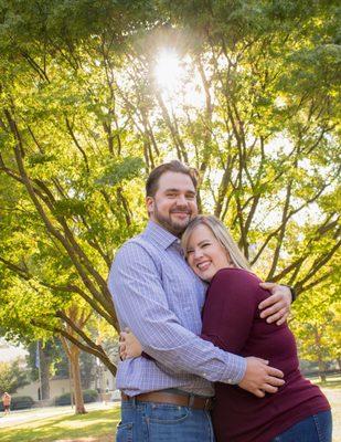 Happy couple embracing under a tree with sunlight streaming through in Sacramento, captured by Cherish the Moment Photography