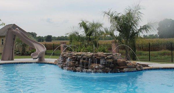 Custom features like this rock wall with water jets and water slide can really enliven your pool!