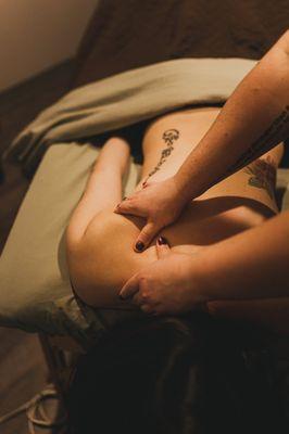 A sports massage therapist works on a client's back and shoulder.