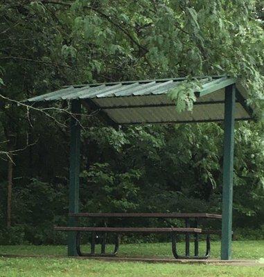 A small shelter in a secluded area near a ball field.