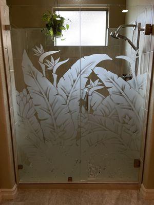 Beautiful tropical frameless shower enclosure offering gorgeous art and privacy at the same time.