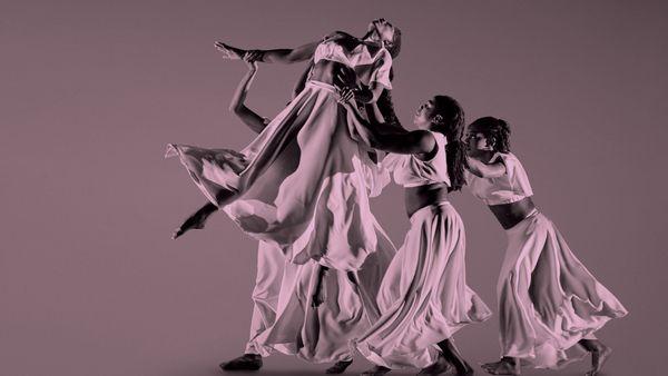 Female dancer lifted by three women in long flowing dresses.