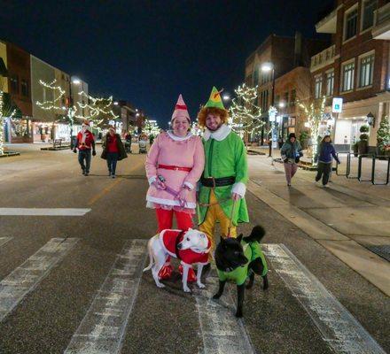 A couple and their dogs, dressed as elves, pose on Main Street for the annual Jingle Bell Fun Run, a free 1-mile holiday run each December