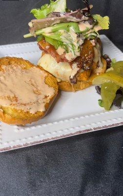 Fried salmon sandwich with special sauce, and a pickle on the side.