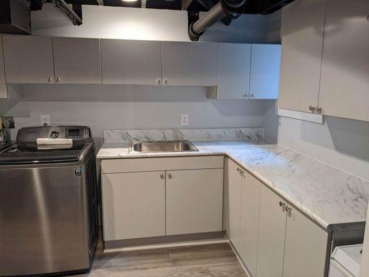 White and chrome laundry room storage cabinets with white marble-like laminate counter top.