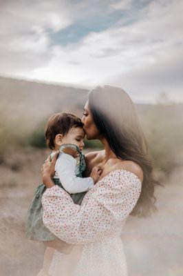 Mom snuggles her toddler among the clouds and mountains