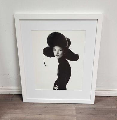 A female model photograph wearing a big hat. Framed with a white mat and white frame with a matte finish.