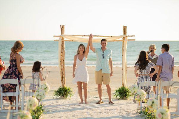 Florida Beach Wedding couple's arms are in the air, as they walk down the aisle of their Fl Beach Wedding.  See our Birch Wood arch & more.