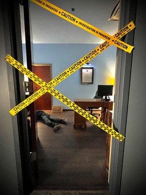 A sneak peak of the CSI escape room with caution tape over the doorway blocking your path.