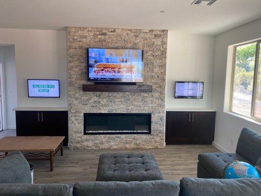 3 TVs symmetrically mounted on wall with fireplace.