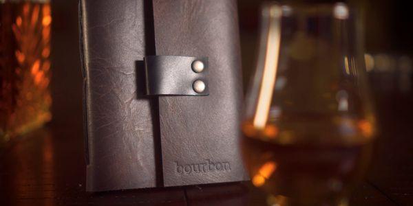 Dynamic product shot of a handmade leather journal with note pages for bourbon tasting.