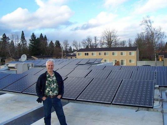 Dr. Dennis W. Clark stands on roof displaying solar panels.