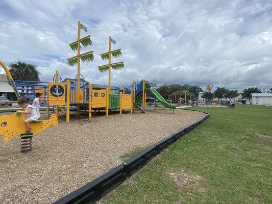 Pirate Ship themed playground with splash pad behind it.